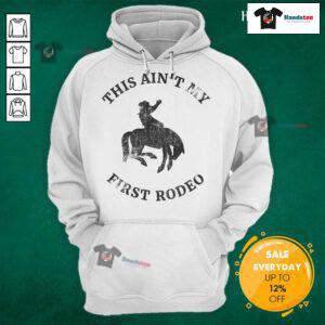 Alt Text: Cowboy wearing an Ain't My First Rodeo hoodie while riding a bronc horse, showcasing rodeo spirit and style.