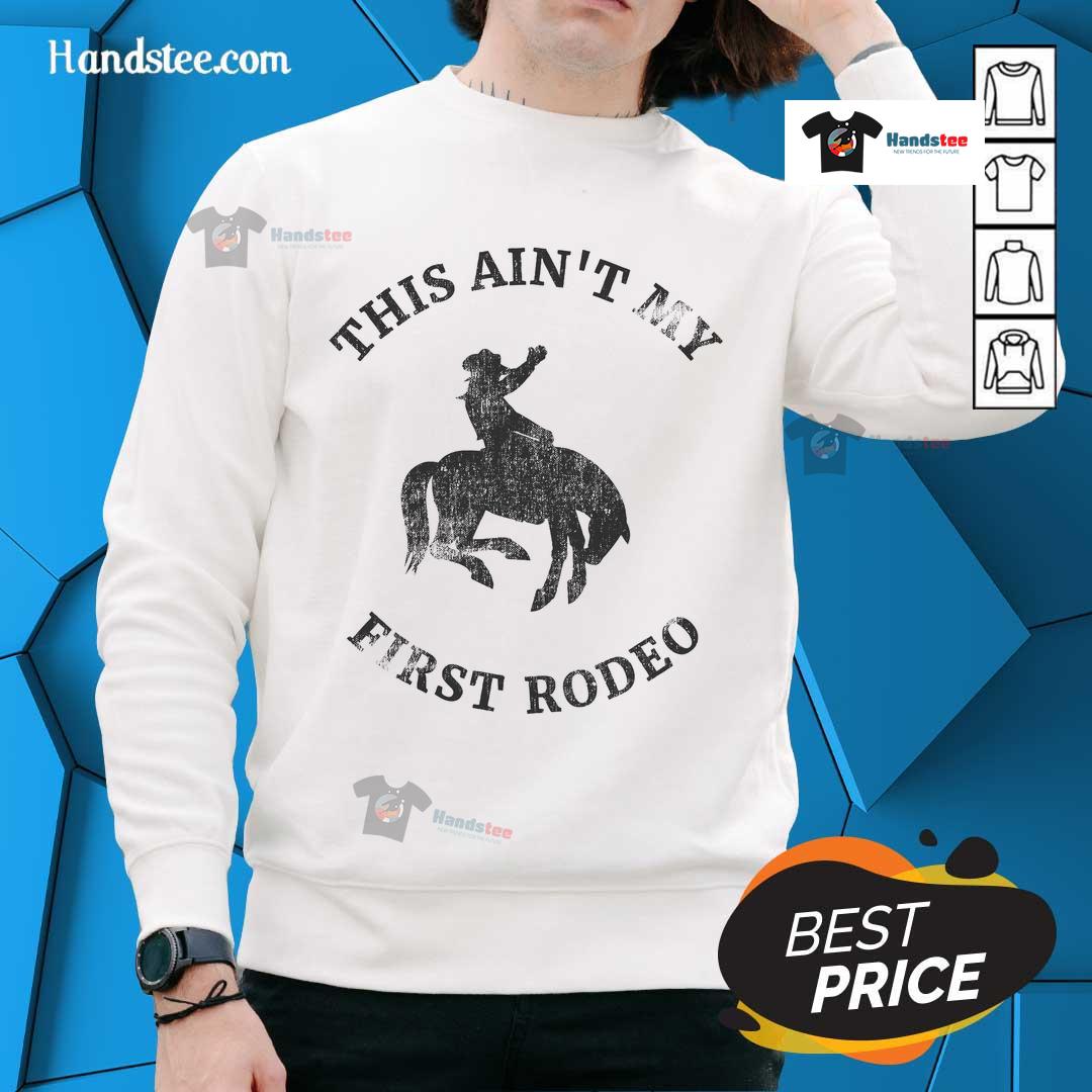 Alt Text: Cowboy wearing an Ain't My First Rodeo sweatshirt, riding a bucking bronc horse at a rodeo event.