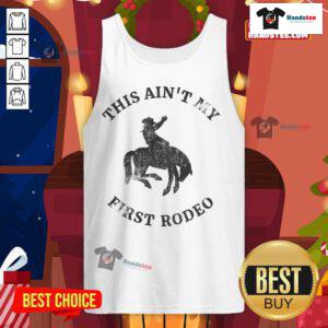 Cool cowboy in 'This Ain't My First Rodeo' tank top riding a bucking bronc at a rodeo event, showcasing western style.