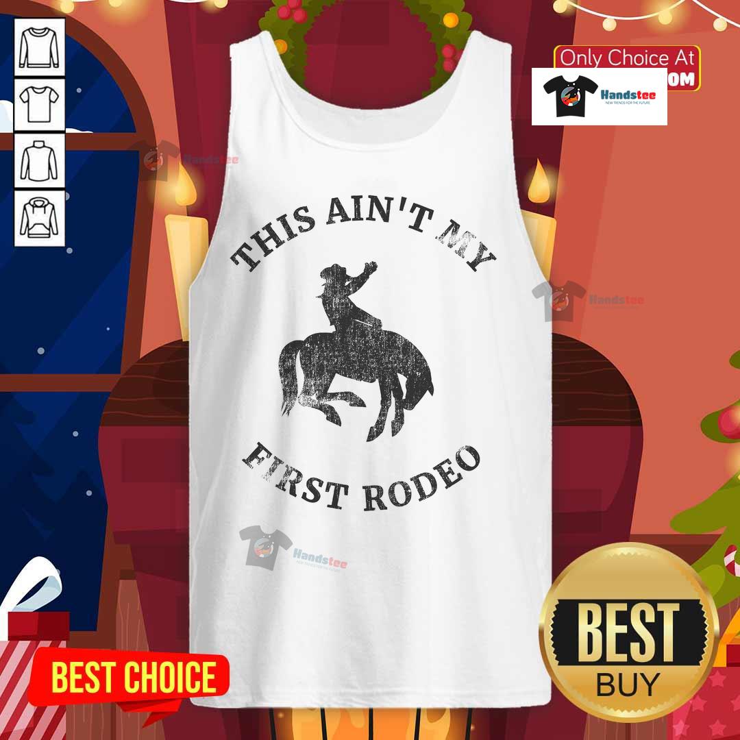 Cool cowboy in 'This Ain't My First Rodeo' tank top riding a bucking bronc at a rodeo event, showcasing western style.