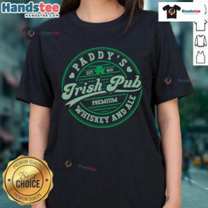 Women in a lively Irish pub celebrate St. Patrick's Day with whiskey and beer, wearing funny Paddy's tees.