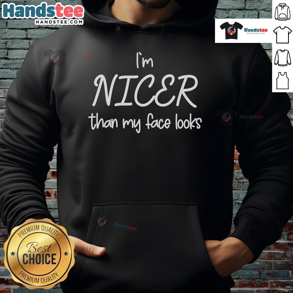 Person wearing 'Good I'm Nicer Than My Face Looks' hoodie, smiling against a vibrant urban backdrop, showcasing trendy streetwear.