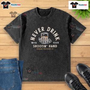 Good Never Drink With Your Shootin Hand Sendero Provisions Co washed t-shirt displayed on a rustic wooden background.