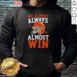 Happy football fan wearing a 'We Almost Always Almost Win' hoodie, showcasing team spirit and humor at a game.