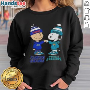Official Charlie Brown fist bump with Snoopy on Florida Gators x Jacksonville Jaguars sweatshirt, perfect for fans.