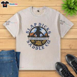 Alt Text: Official Ain't Gonna Ride Itself Slap Dicks Saddle Co Logo on a washed t-shirt, perfect for casual wear.